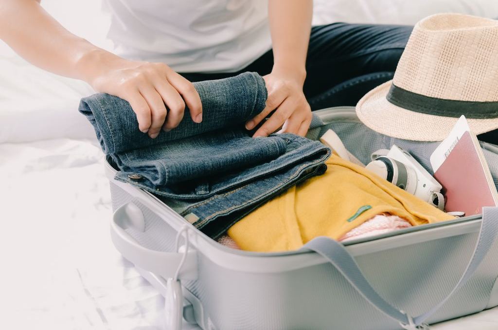 Close up of a packed suitcase with clothes and a person putting jeans in.