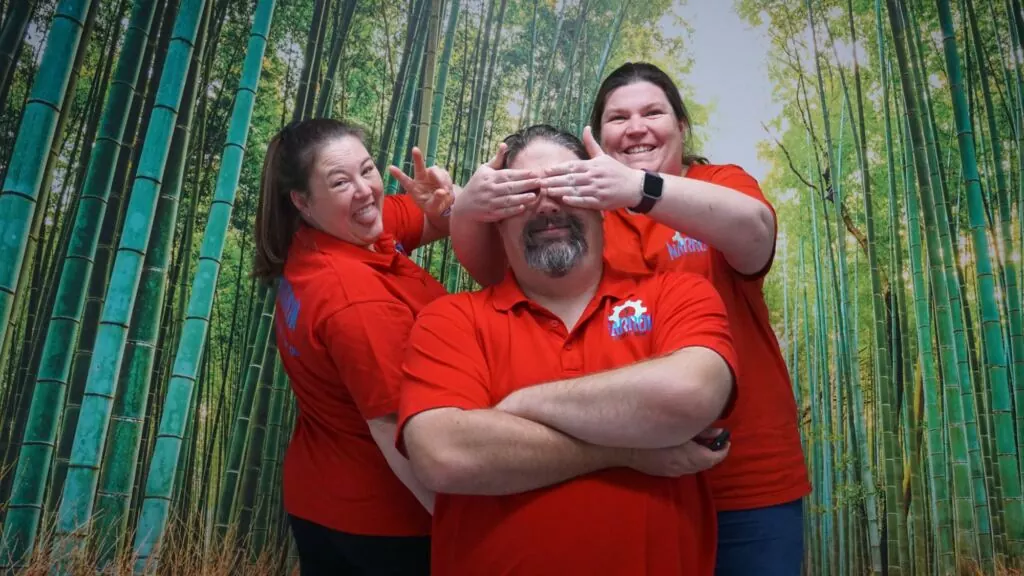 The Narrow Escape Rooms Penrith owners in front of a bamboo forest poster smiling at being cheeky.